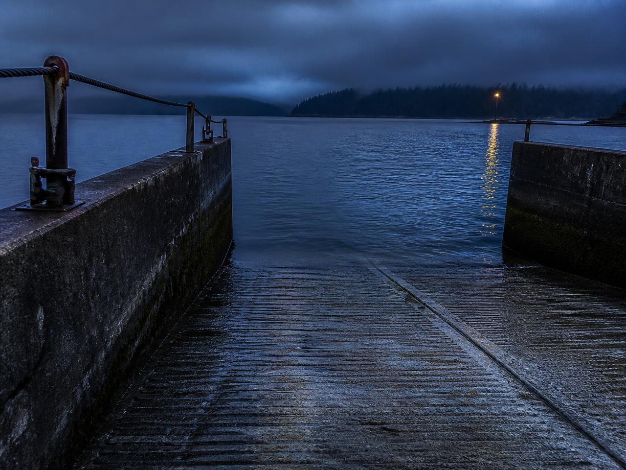 A wet public boat ramp descending into cold water before dawn